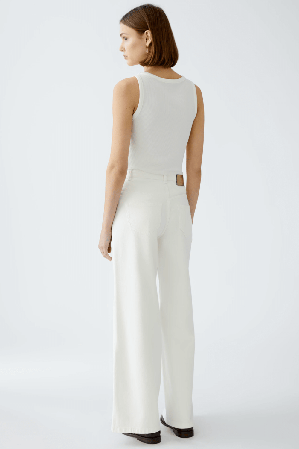 Femme vue de dos portant un jean blanc taille haute et un débardeur, affichant un look moderne et décontracté.