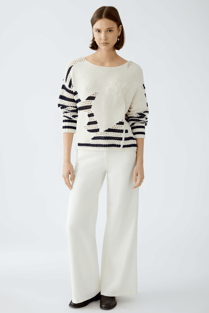 Femme en pull à rayures blanches et noires, pantalon blanc large, look contemporain et élégant.