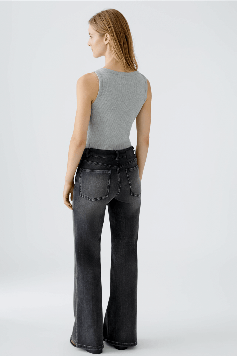 Femme vue de dos portant un tank top gris et des jeans évasés en denim noir, mettant en avant leur coupe moderne.