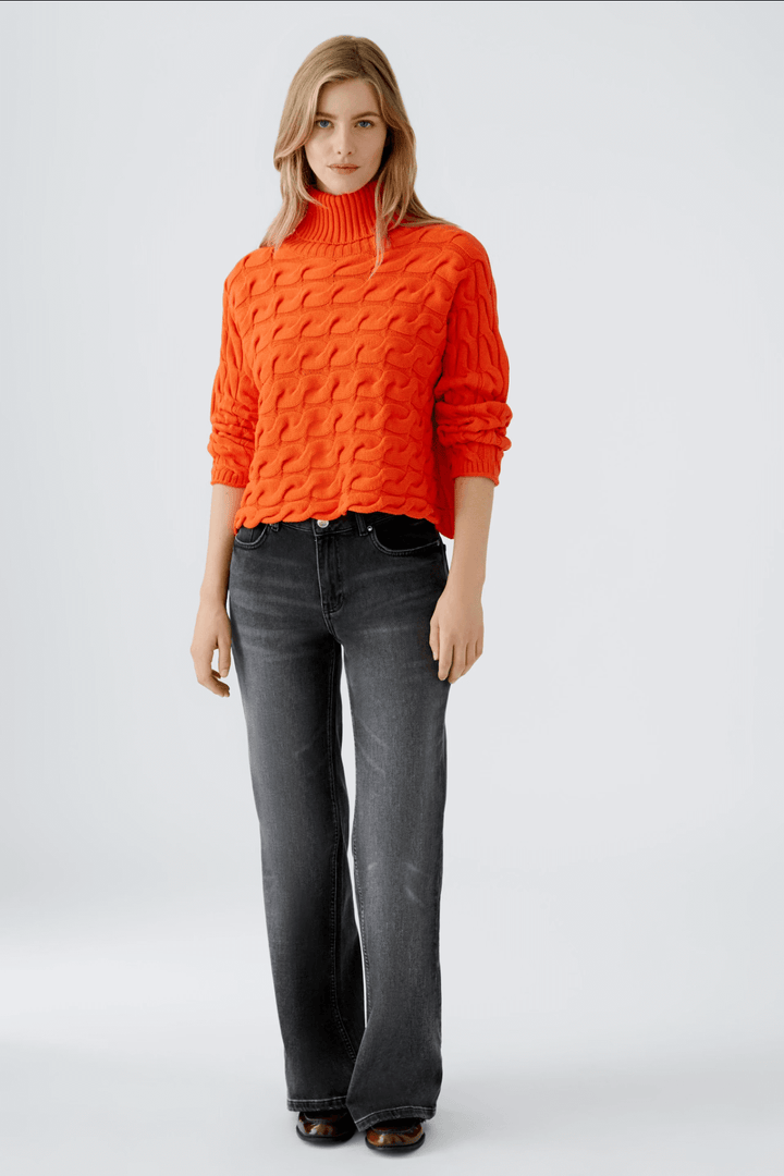 Femme portant un pull orange à col montant et un jean évasé noir, look décontracté et moderne.
