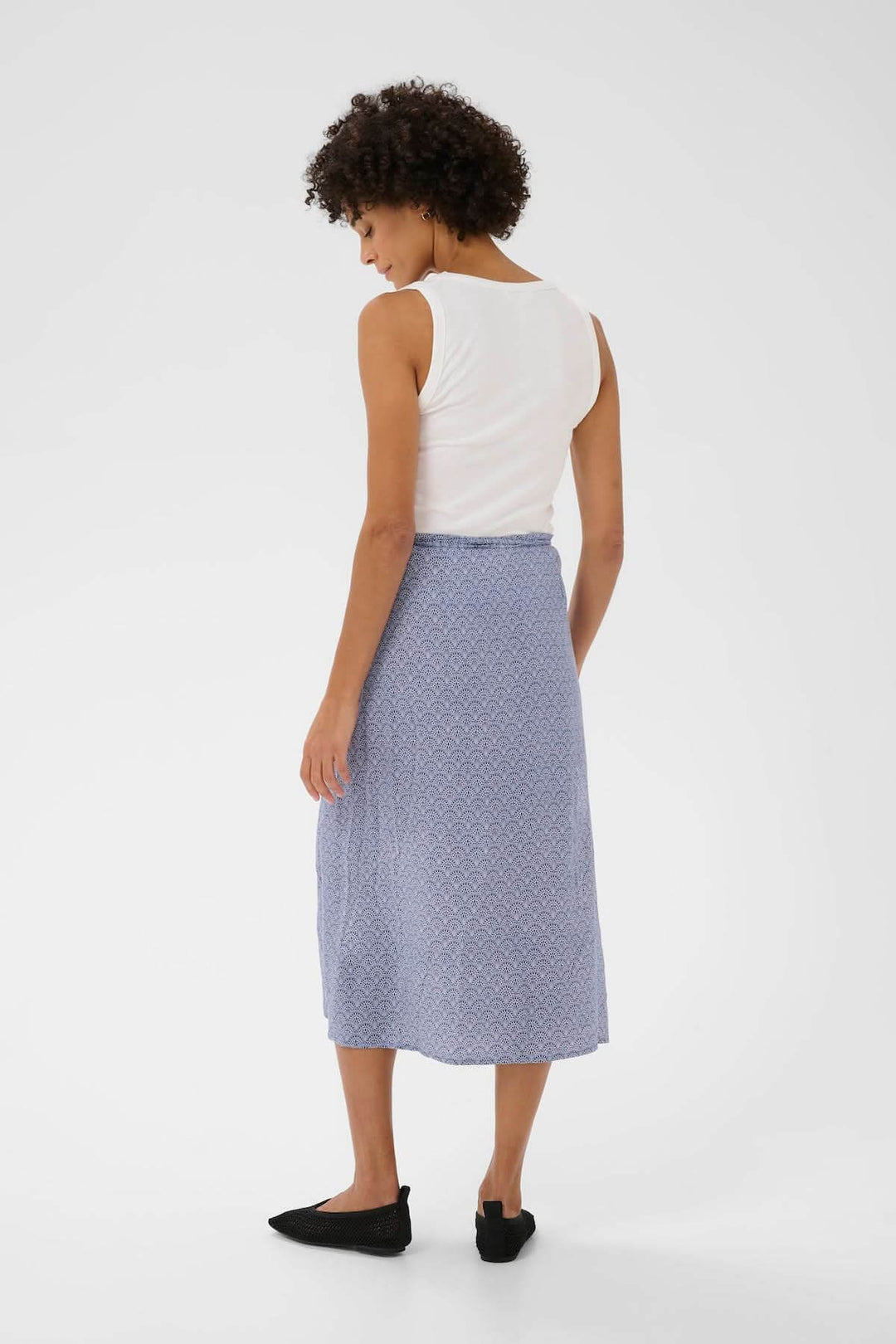 Femme portant une Jupe Arielle midi bleue fluide avec imprimé délicat et taille ajustable, vue de dos.