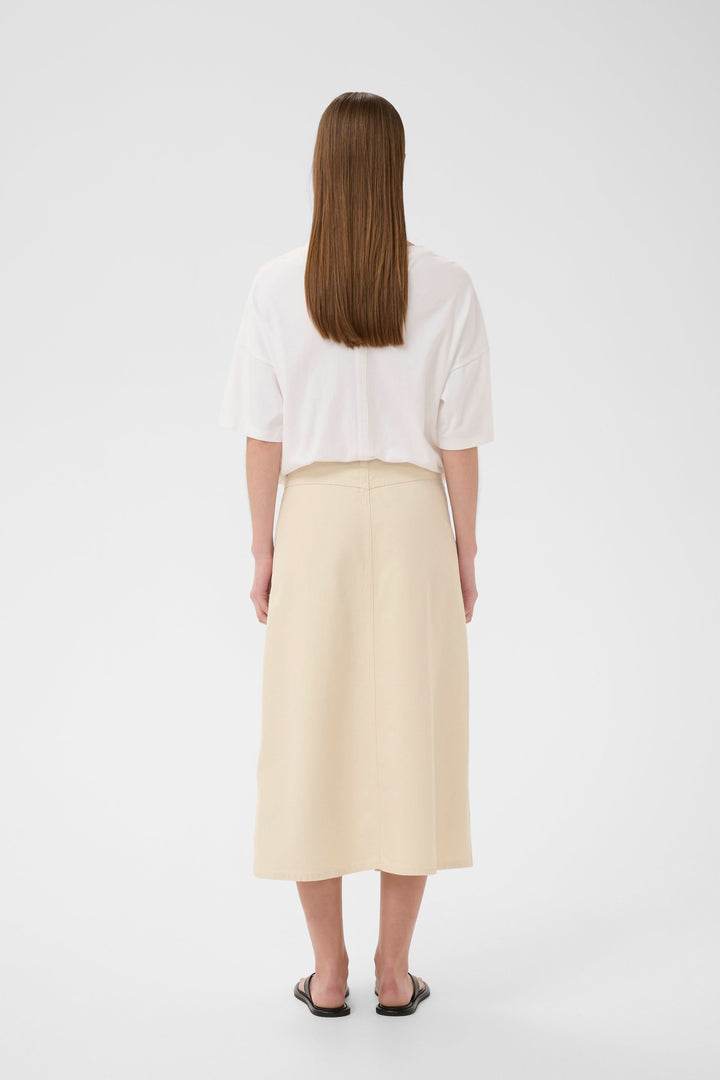 Vue arrière de la Jupe Dilys midi droite à poches plaquées, couleur beige, portée par une femme, style moderne et minimaliste.