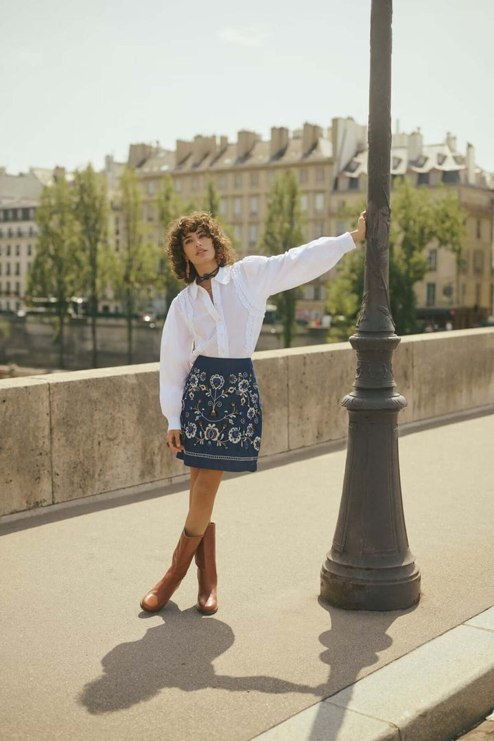 Femme portant une Jupe Gro en denim avec broderies florales, décontractée et élégante, contre un paysage urbain.