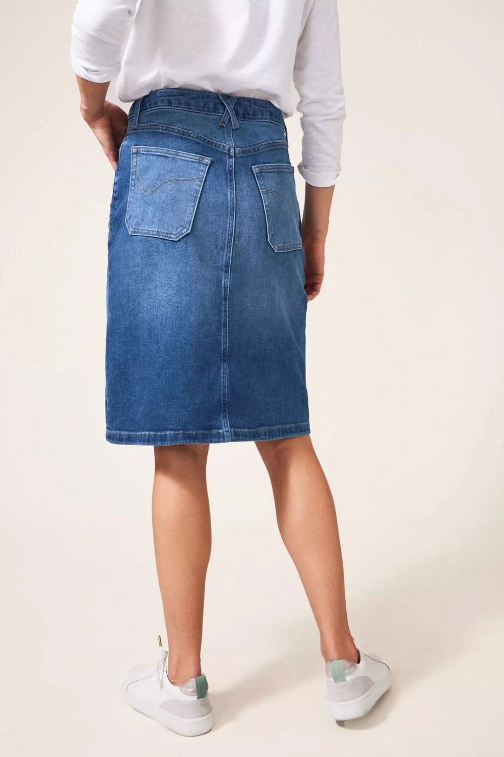 Vue arrière d'une jupe midi en jean, portée avec un tshirt blanc et des baskets blanches.