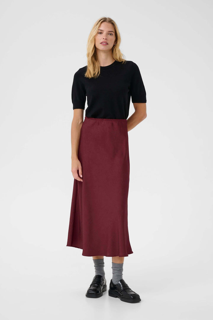 Femme portant une jupe midi fluide bordeaux, avec un chandail noir, dans un style élégant et moderne.