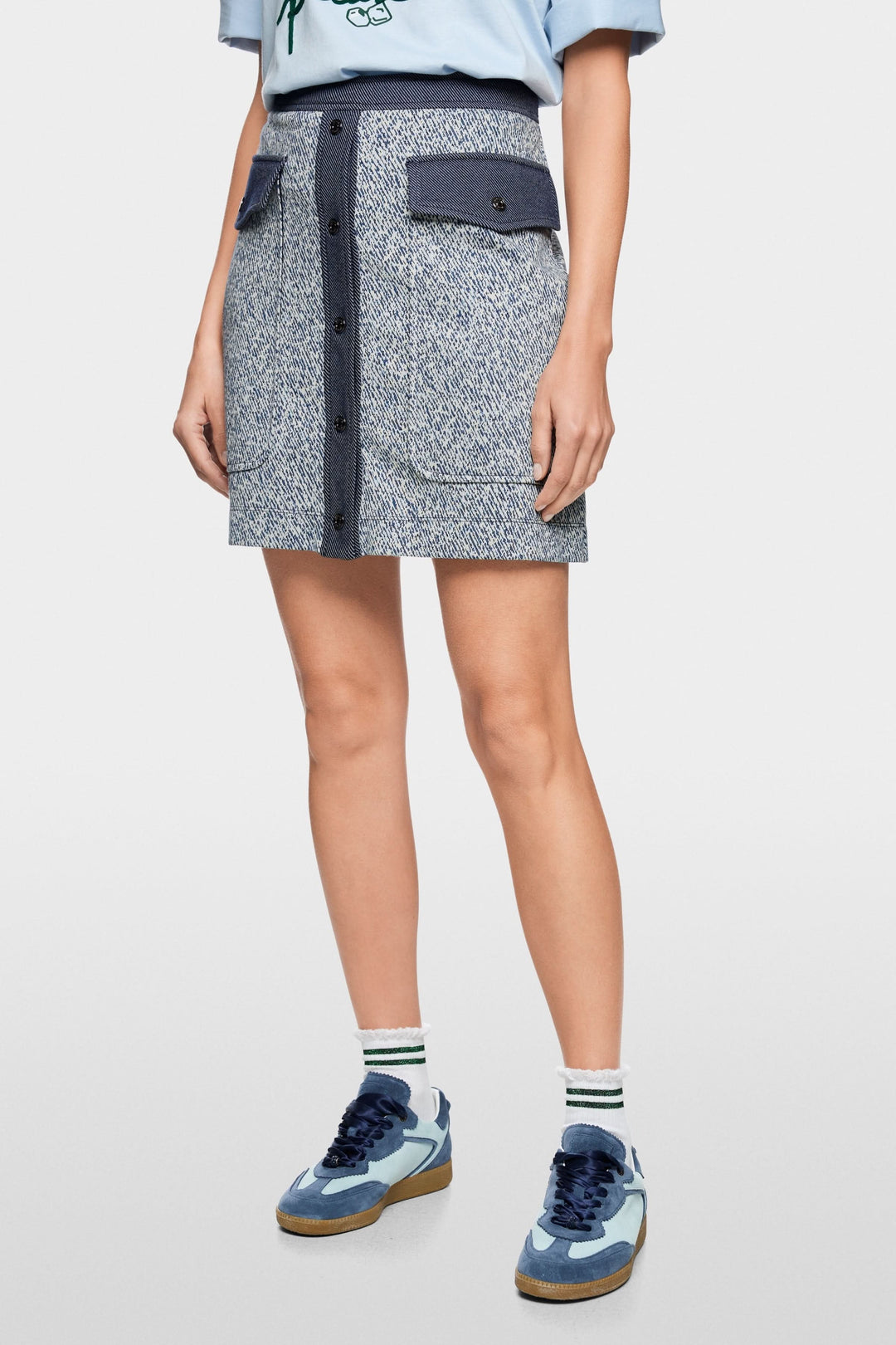 Femme portant une jupe courte en viscose extensible avec boutons et poches à rabat, style utilitaire moderne.