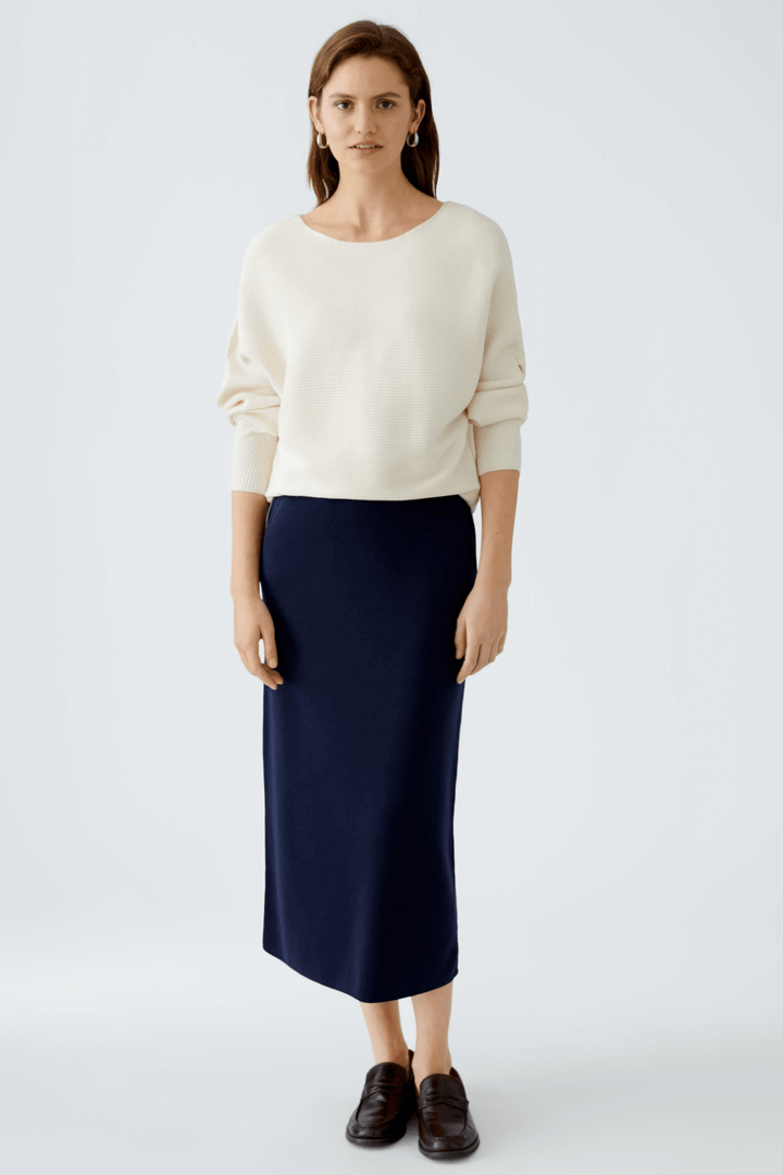 Femme portant une jupe droite en tricot navy avec un pull beige, style chic et décontracté.