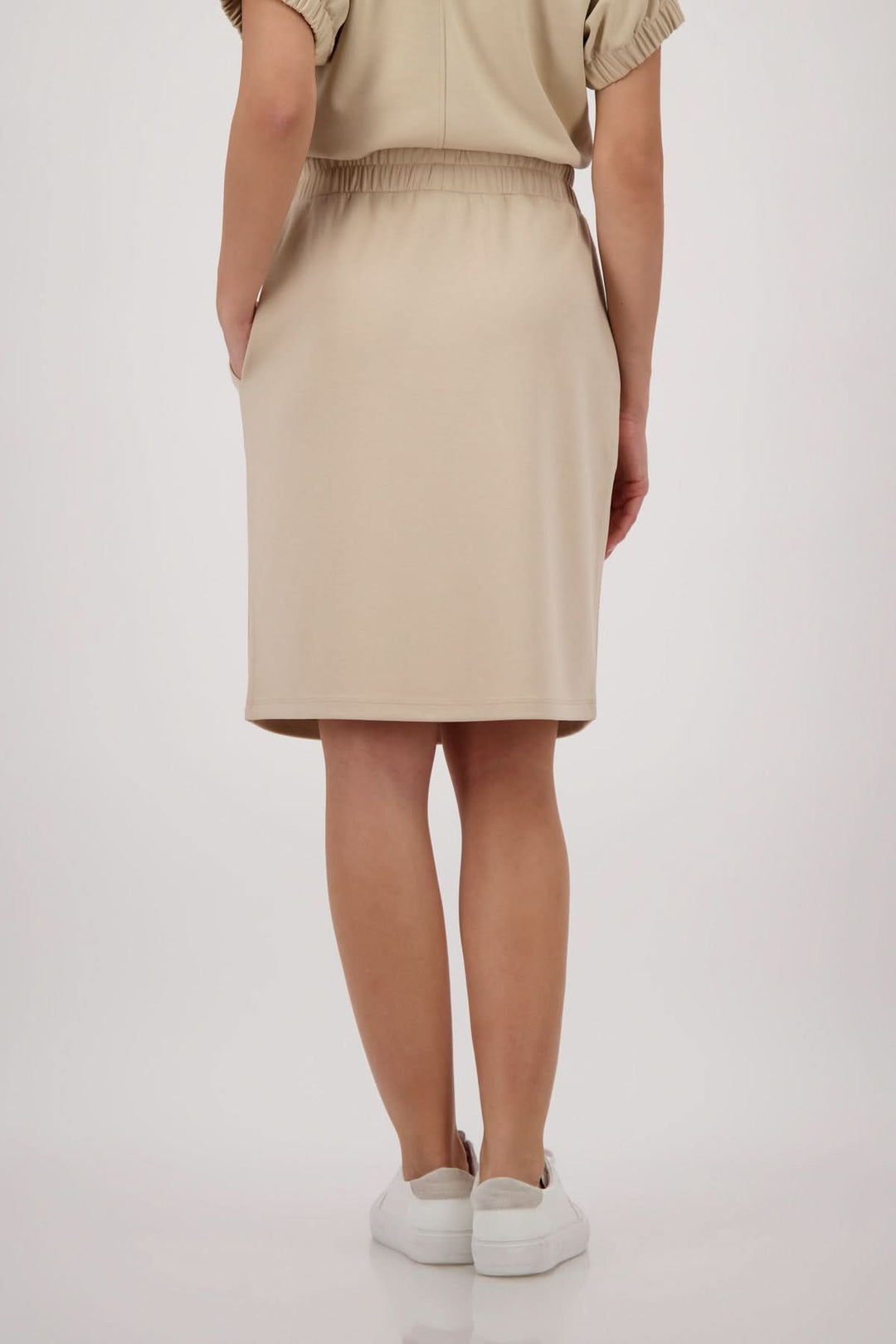 Vue arrière de la jupe droite à taille élastique beige, portée par une femme, mettant en évidence le style épuré et contemporain.