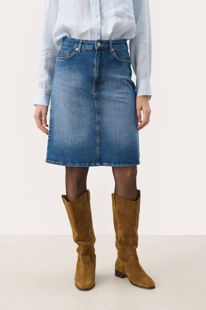 Jupe en denim classique Leja avec coupe flatteuse, portée avec une chemise et des bottes marron.