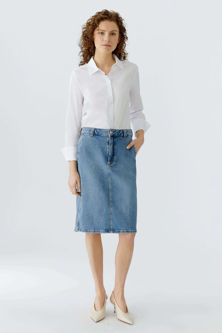 Jupe en denim classique portée avec une blouse blanche, offrant une silhouette élégante et intemporelle, idéale pour un style polyvalent.
