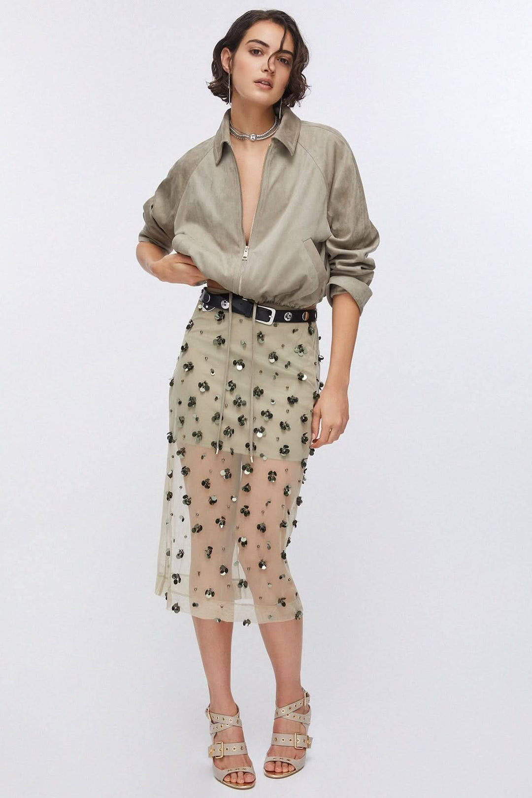 Femme portant une jupe en maille transparente ornée avec applications décoratives, tenue élégante et moderne, cadre blanc.