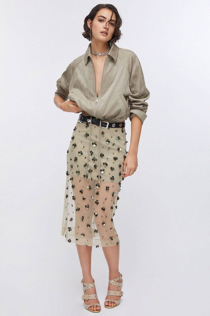 Femme portant une jupe en maille transparente ornée avec applications décoratives, tenue élégante et moderne, cadre blanc.