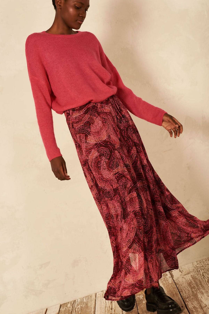 Une femme portant une jupe longue fluide à imprimé abstrait, associée à un pull rose.