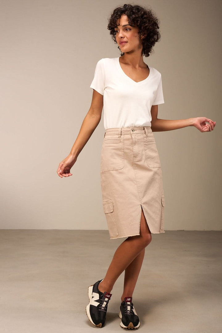 Jupe midi ajustée beige avec poches plaquées, ourlet effiloché et fente, portée avec un t-shirt blanc.