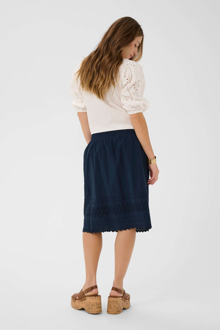 Femme portant une jupe midi brodée à taille élastique avec ourlet festonné et broderie ajourée, vue de dos.