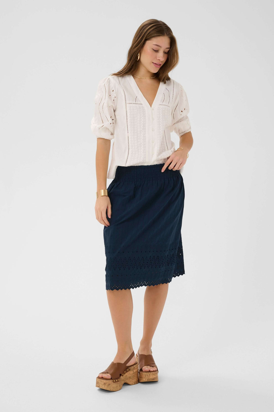 Femme portant une jupe midi brodée à taille élastique avec ourlet ajouré et finition festonnée, idéale pour la saison chaude.