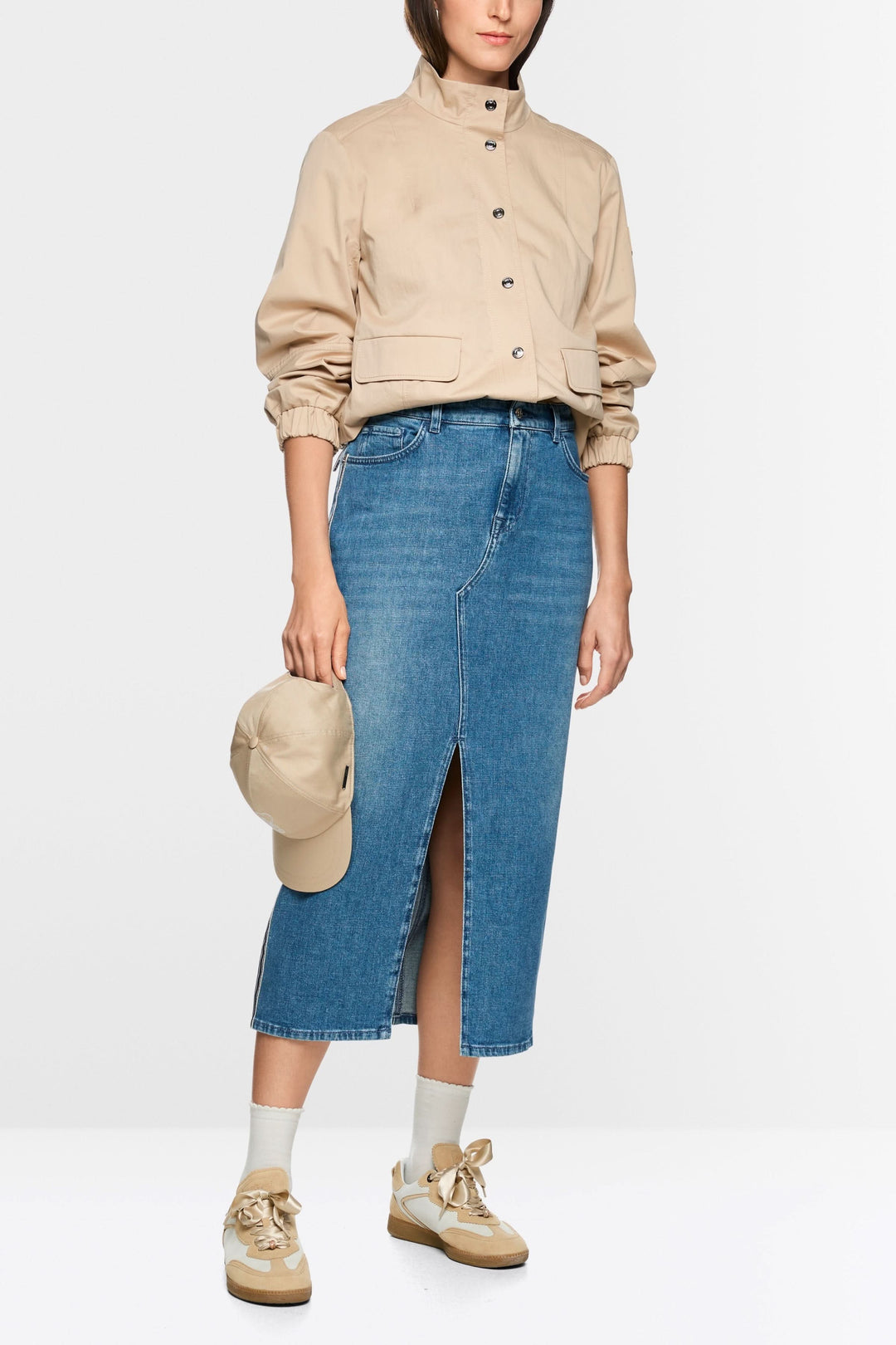 Jupe midi en jean à rayures latérales avec fente avant, portée avec une veste beige et des baskets dorées.