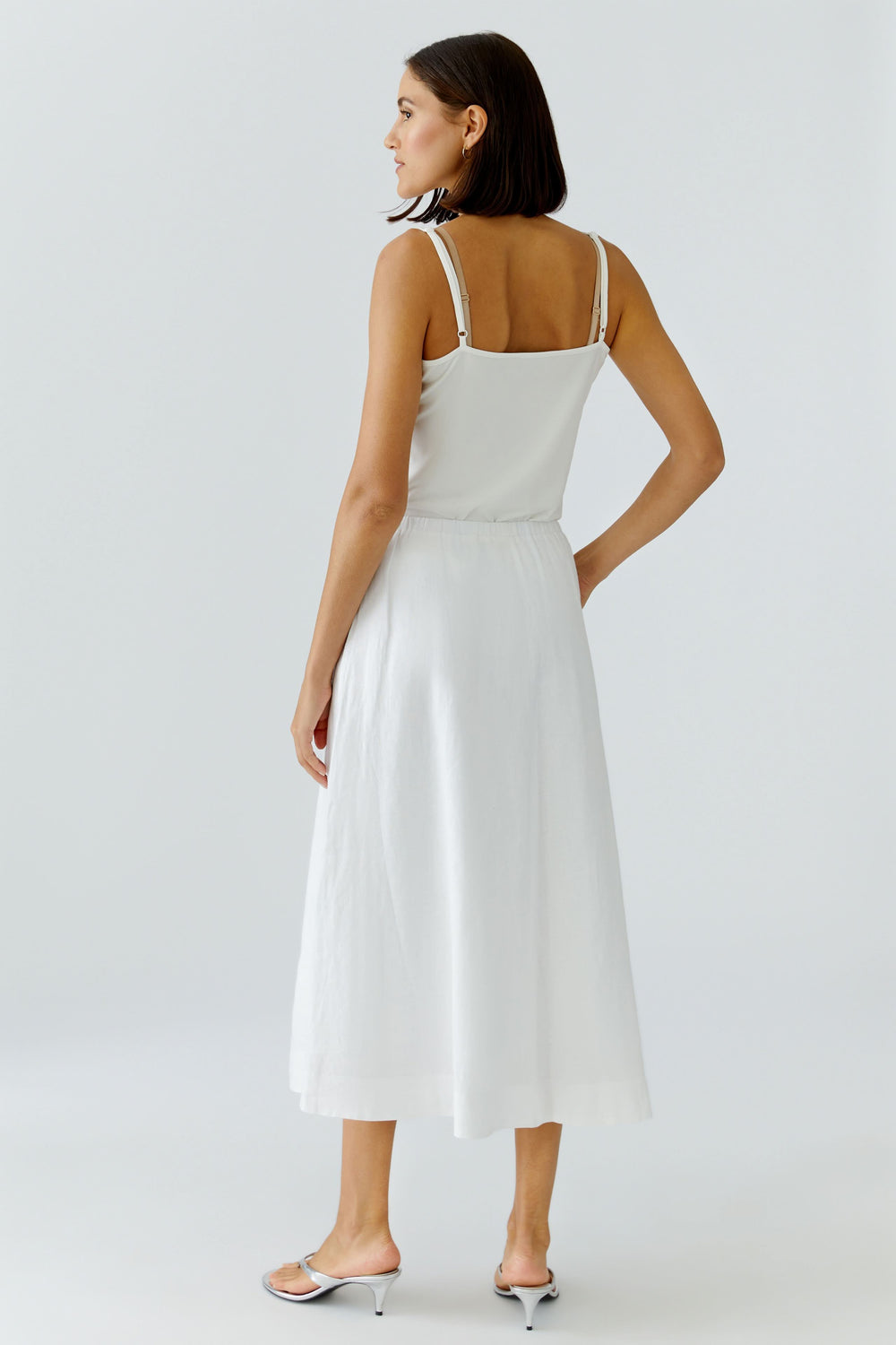 Jupe midi fluide blanche portée par une modèle de dos, montrant sa coupe élégante et sa longueur mi-mollet, idéale pour un style féminin.
