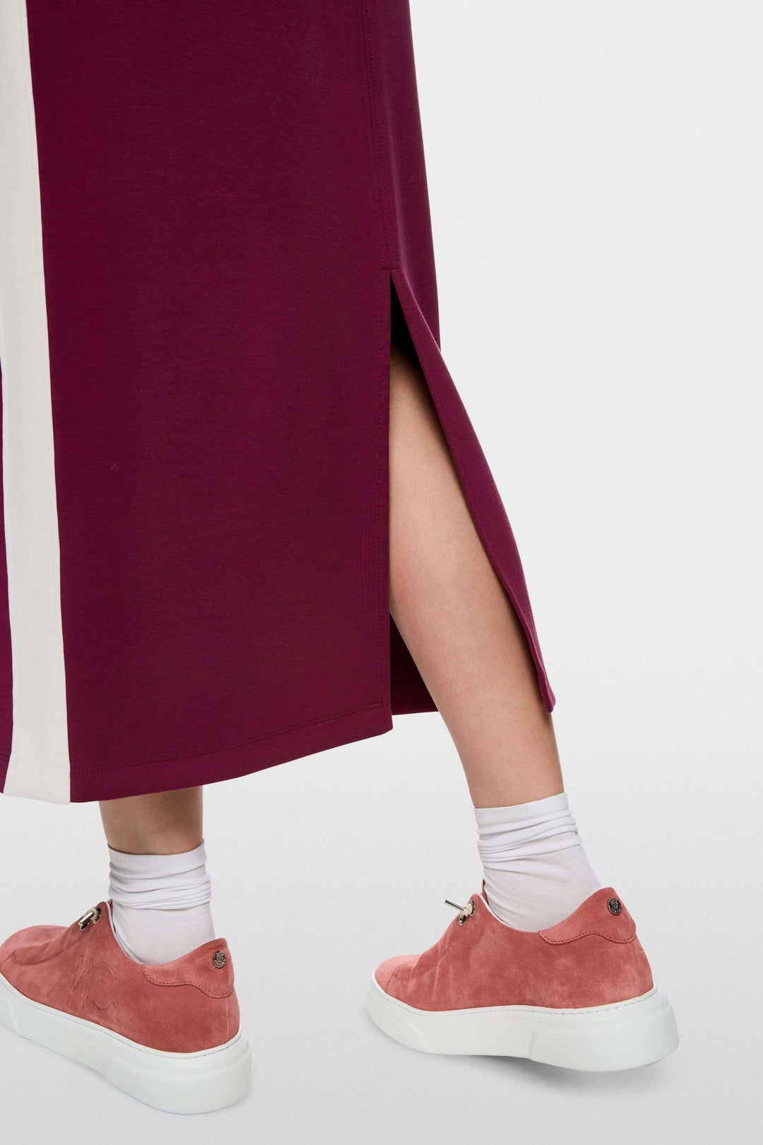 Gros plan sur la jupe midi sportive avec fente arrière, bandes contrastées et sneakers roses visibles, Marc Cain Sports.