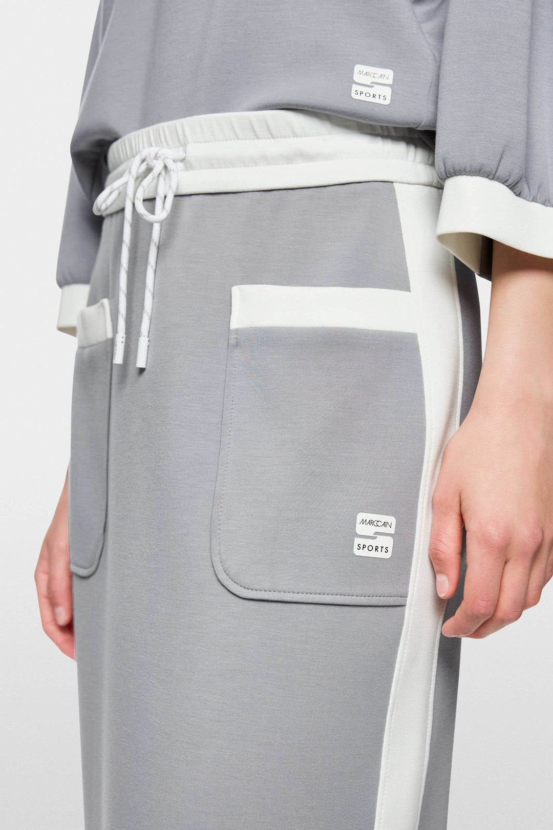 Jupe midi sportive grise avec poches contrastées et taille élastique, logo Marc Cain Sports visible, fente arrière pour mouvement.