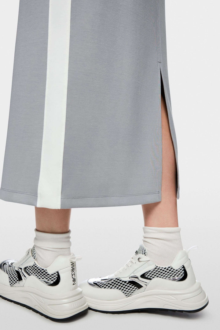 Détail de la jupe midi sportive avec fente à l'arrière, bandes contrastées et baskets blanches, logo Marc Cain visible.