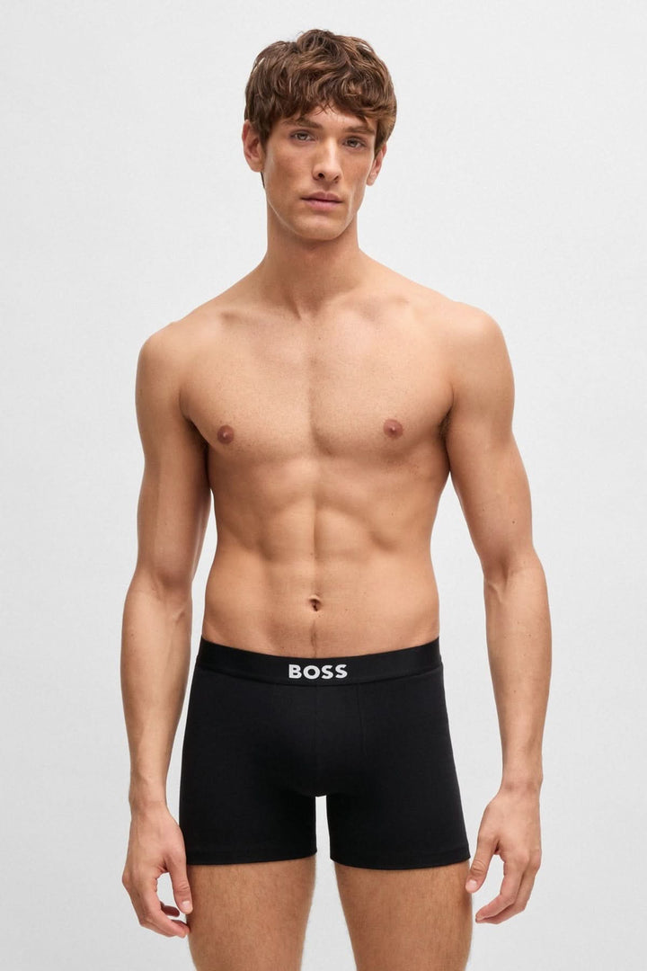 Homme portant des boxers noirs BOSS avec ceinture logo, présentés dans une pose élégante.