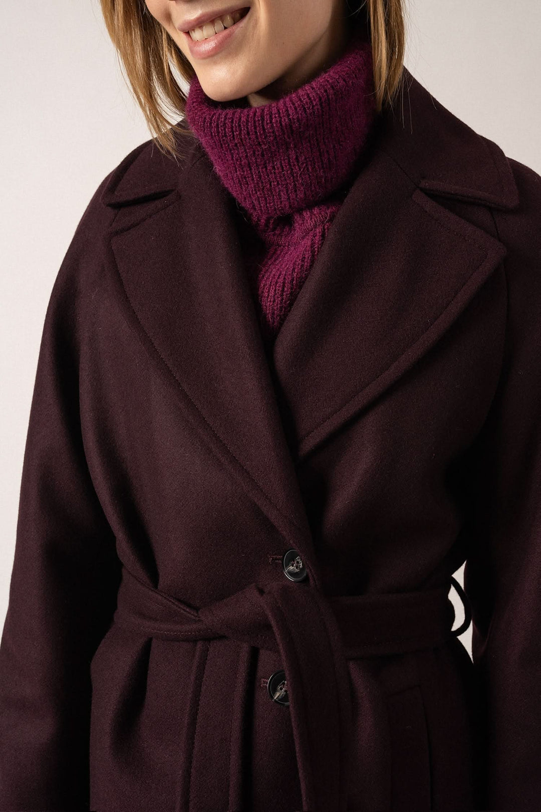 Manteau St-Enora en tissu de laine, ceinture ajustable, élégant et confortable, porté avec un pull à col roulé.