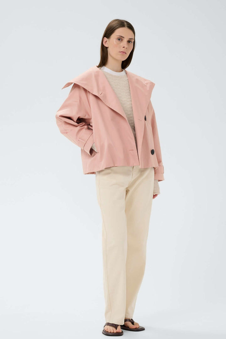 Femme portant le Manteau court Mazie rose avec col évasé et fermeture à 3 boutons, intégré à une tenue décontractée avec pantalon crème.