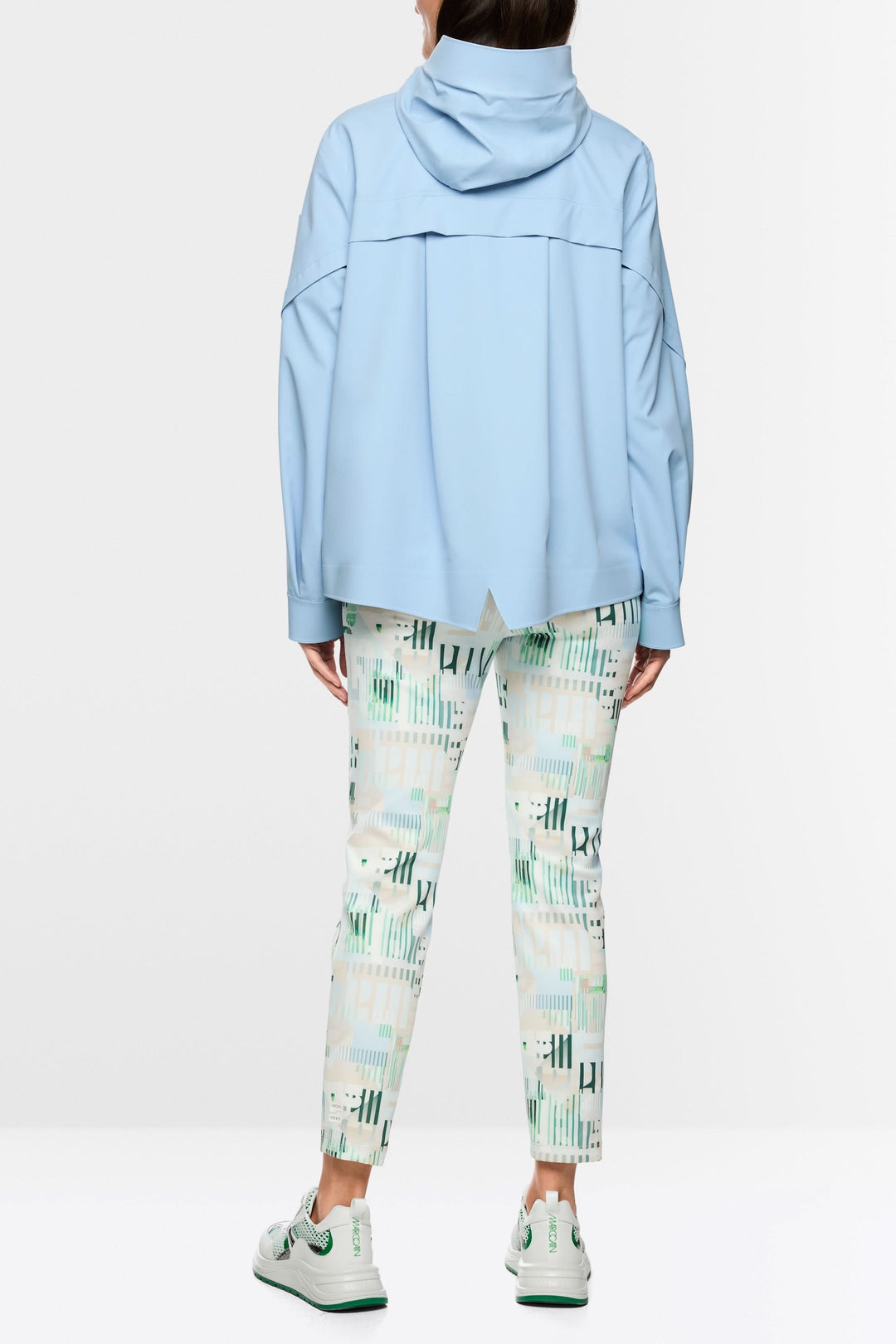 Vue arrière du manteau d'extérieur léger avec capuche bleue, coupe moderne, porté avec un pantalon imprimé graphique.