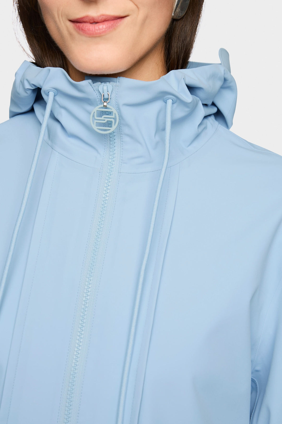 Femme portant un manteau d'extérieur léger avec capuche bleu, fermeture à glissière, idéal pour mi-saison, coupe élégante et moderne.