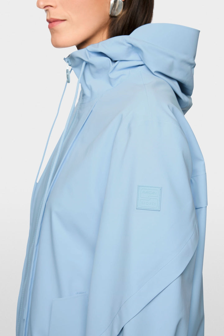 Femme portant un manteau d'extérieur léger avec capuche, couleur bleu ciel, avec fermeture à glissière et coupe épurée.