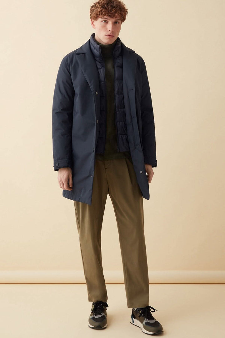 Homme portant un manteau long en tissu recyclé, affichant un look métropolitain et sportif.