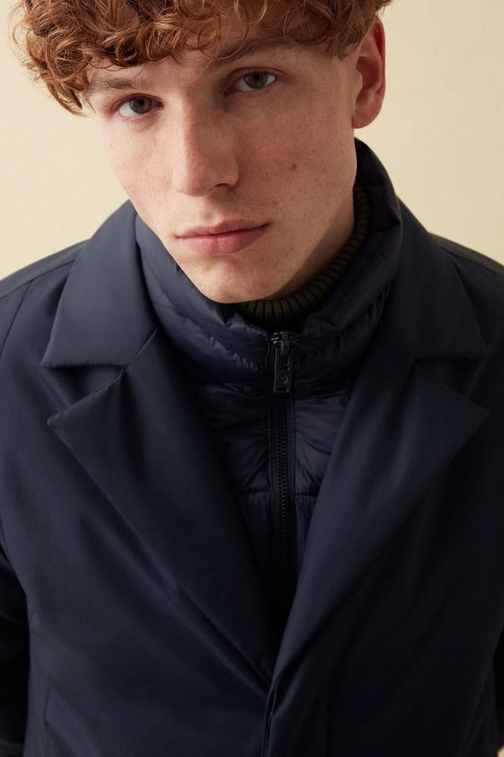 Homme portant un manteau long en tissu recyclé, look métropolitain, avec fermeture éclair et col côtelé.