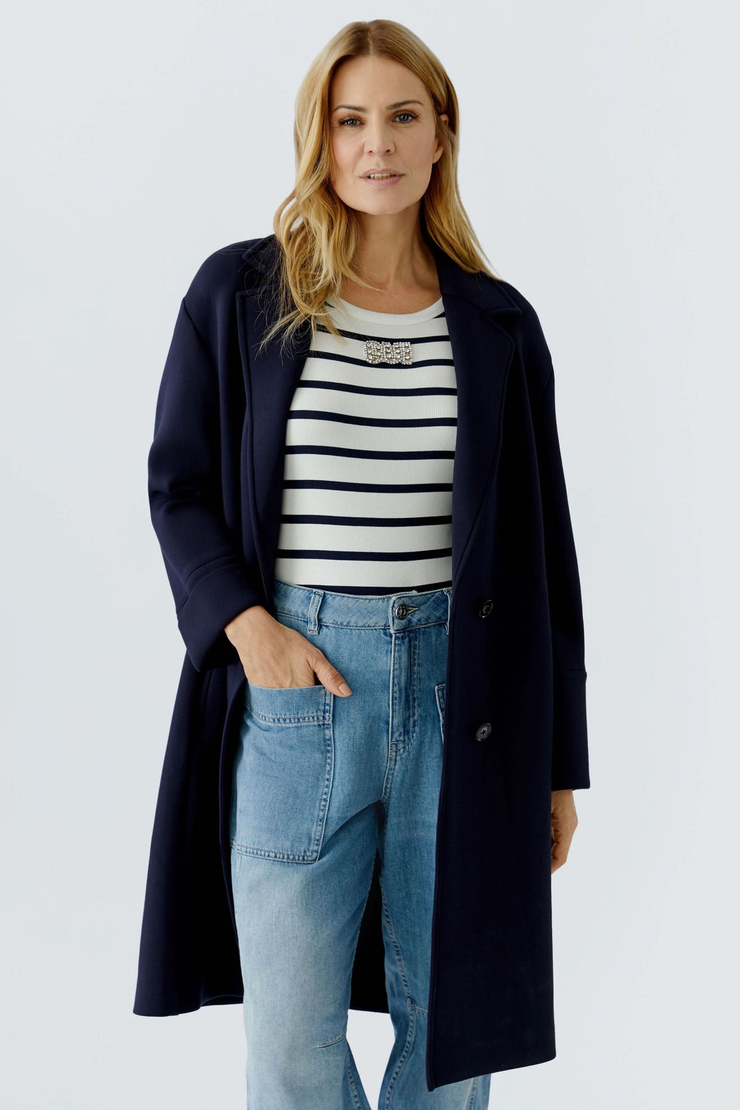 Femme portant un manteau long à coupe droite, design épuré, avec col tailleur classique, convenant à une tenue élégante et structurée.