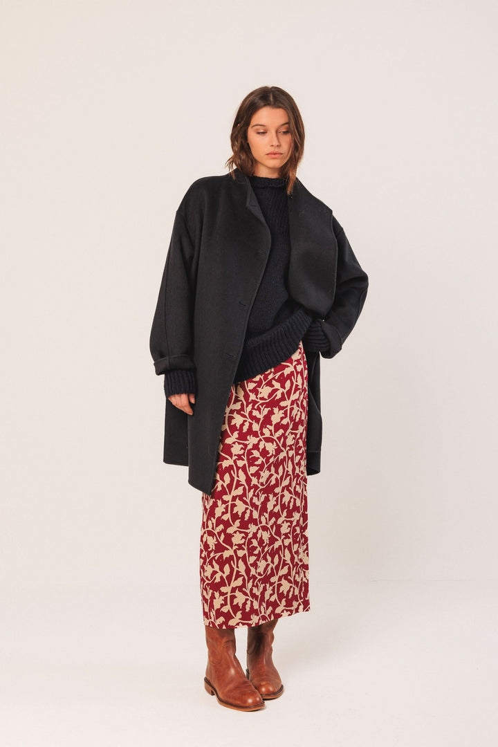 Manteau minimaliste élégant avec coupe oversize, porté sur une robe fleurie, style moderne et raffiné.
