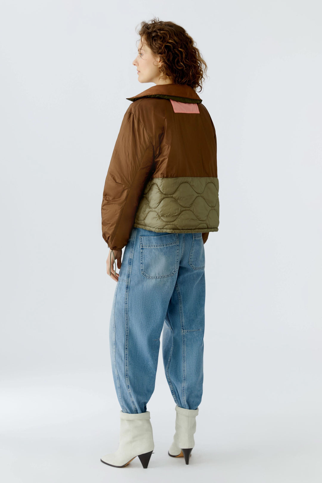 Femme portant un manteau réversible matelassé avec faces contrastantes, jeans décontracté, et bottes blanches, vue arrière.