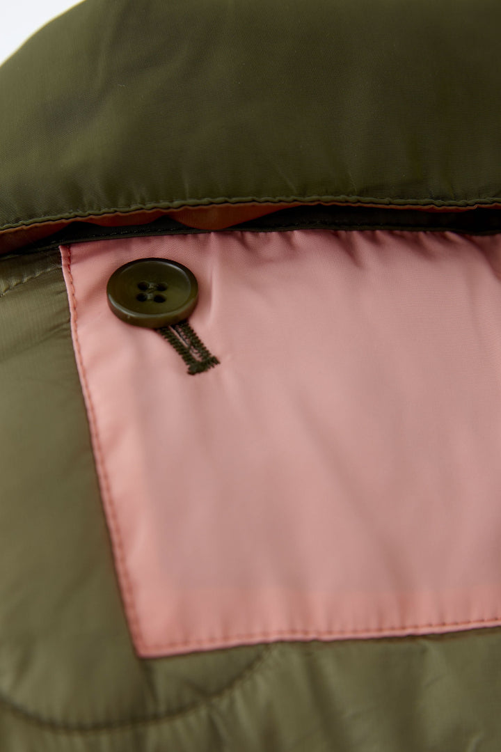 Gros plan sur le bouton du manteau réversible matelassé avec faces rose et kaki, combinant style et fonctionnalité.