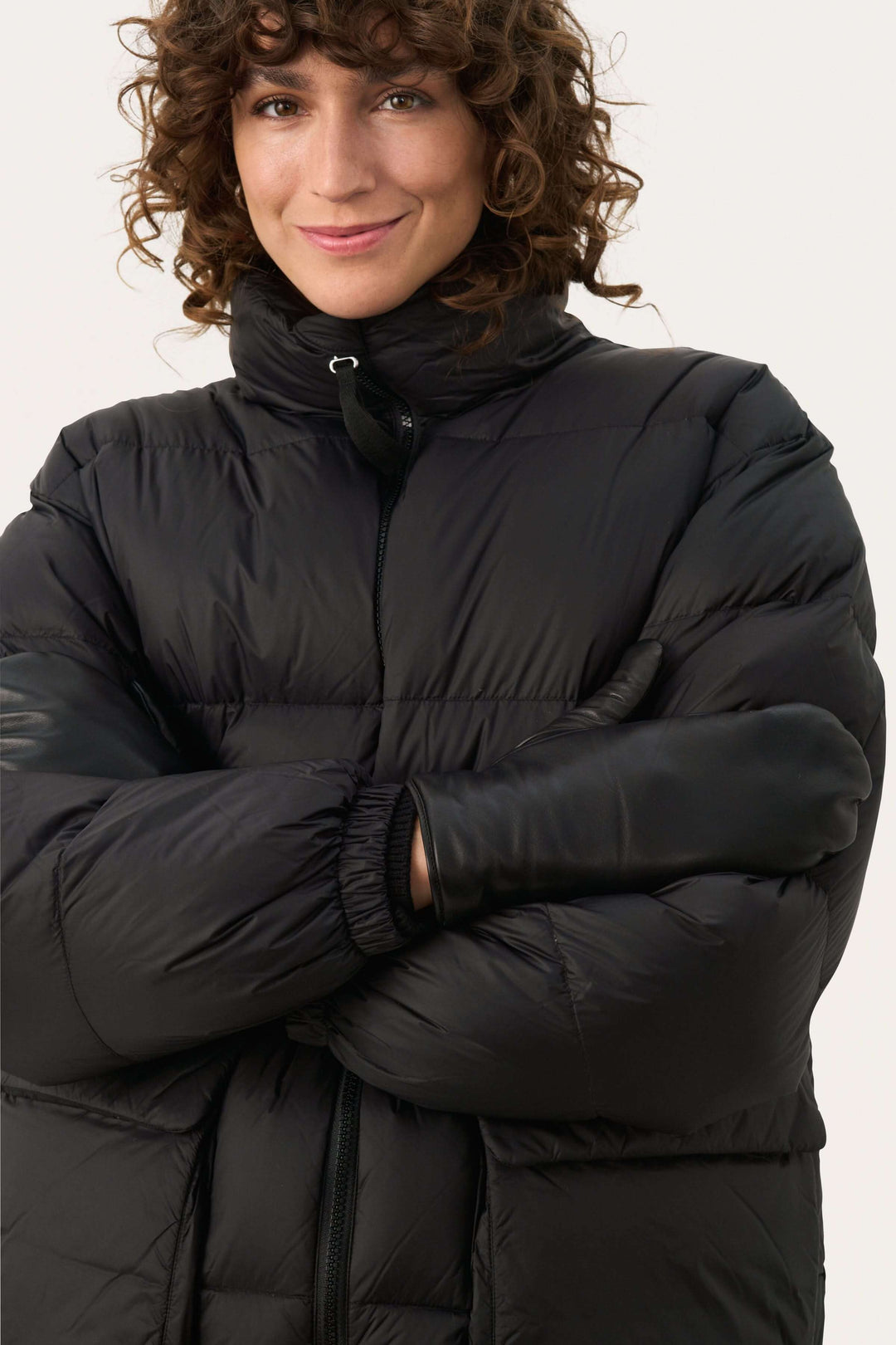 Femme souriante portant un manteau noir en duvet et des mitaines en cuir, prête pour l'hiver.