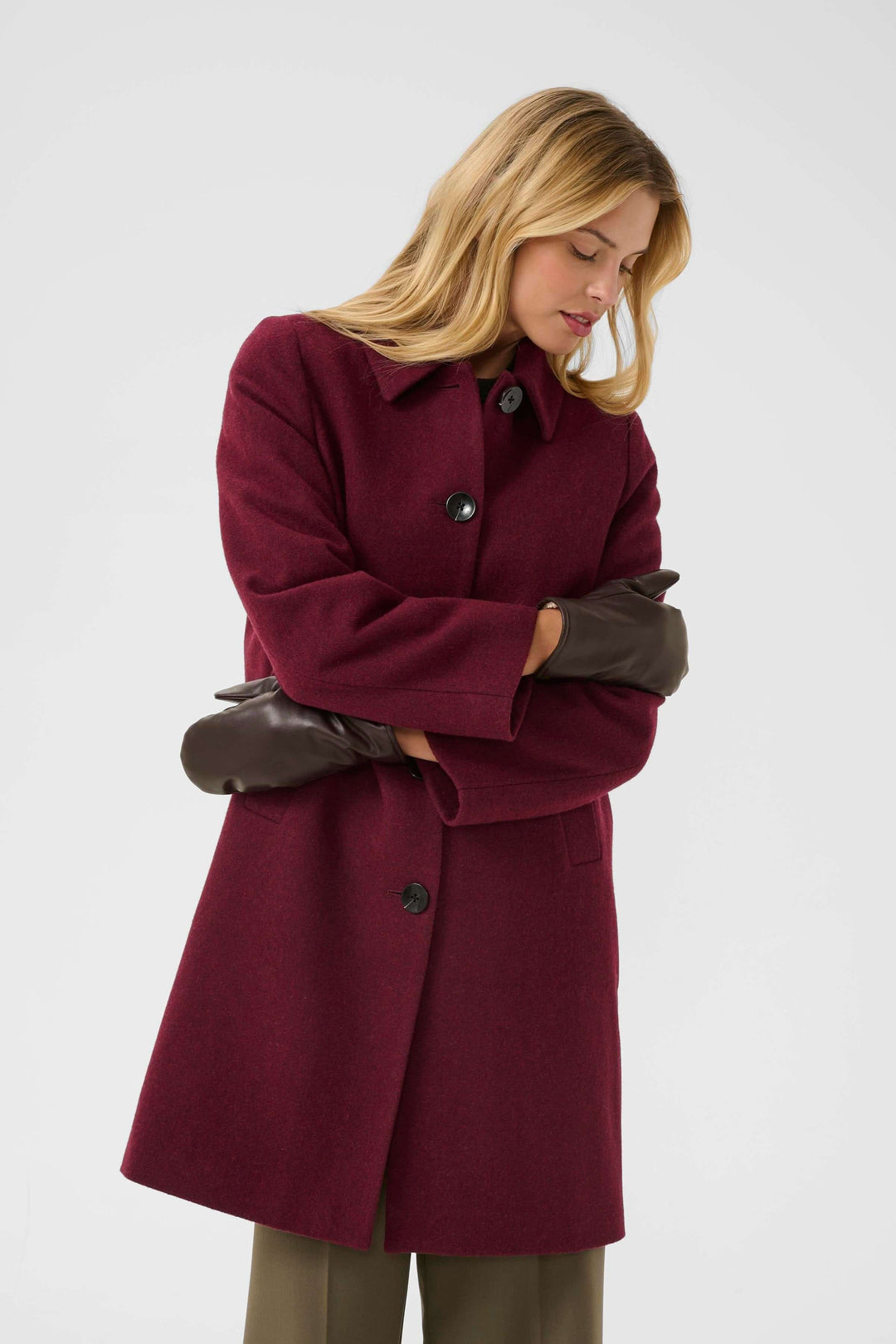 Femme portant un manteau bordeaux élégant avec des mitaines en cuir, le style hivernal parfait.
