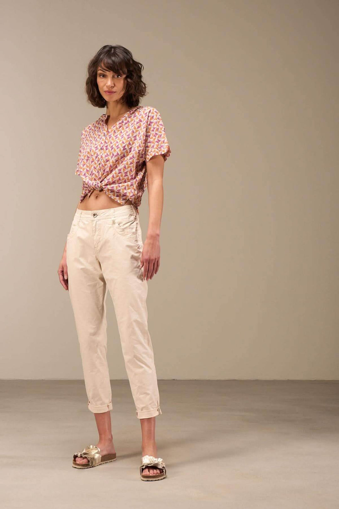 Femme portant un pantalon 7/8 moulant beige, avec un haut à motifs colorés et des sandales, en studio.