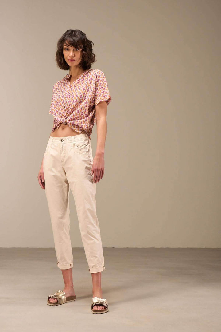 Femme portant un pantalon 7/8 moulant beige, avec un haut à motifs colorés et des sandales, en studio.