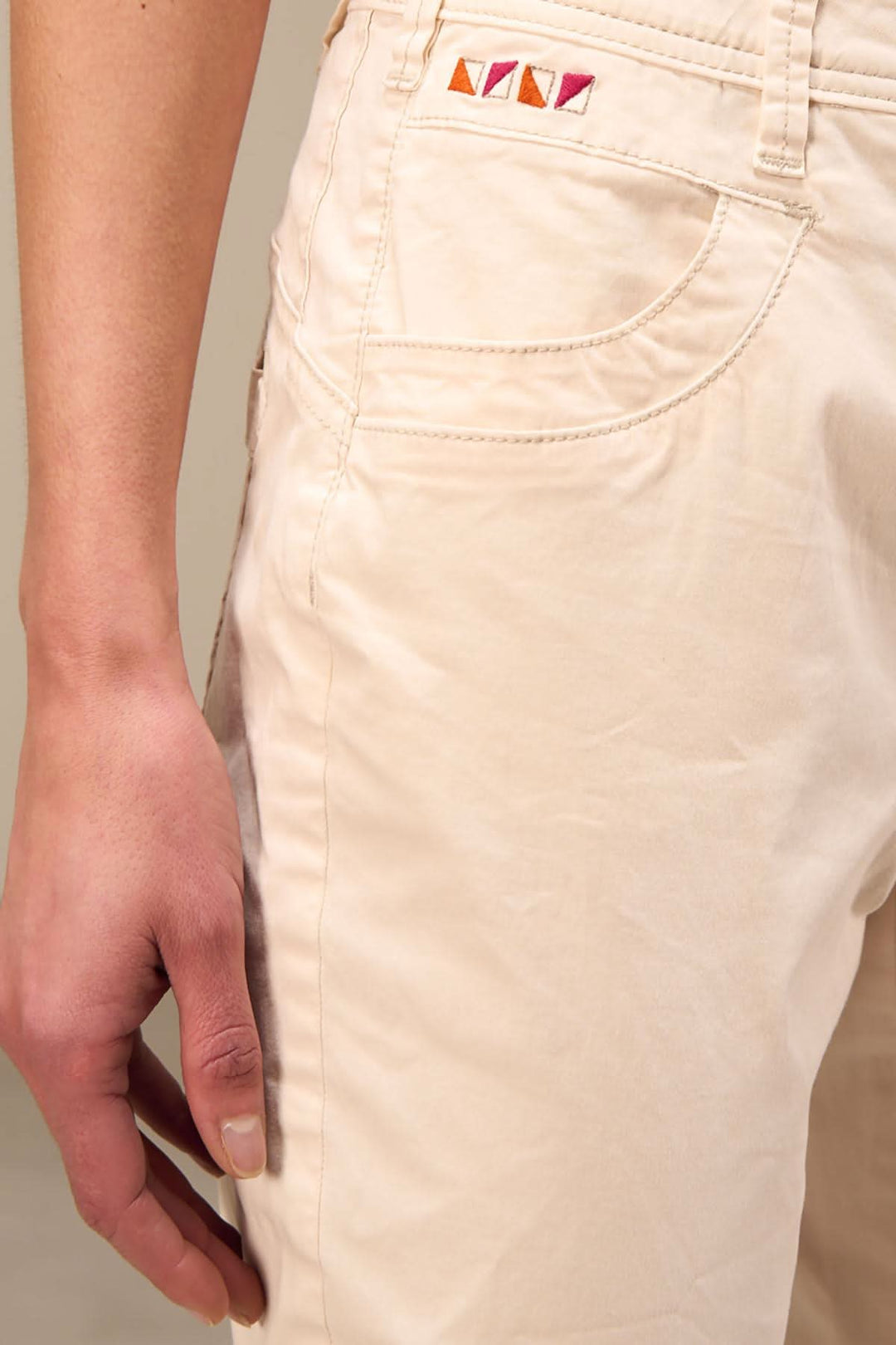 Détail sur le pantalon 7/8 beige avec poche arrière et surpiqûres colorées.