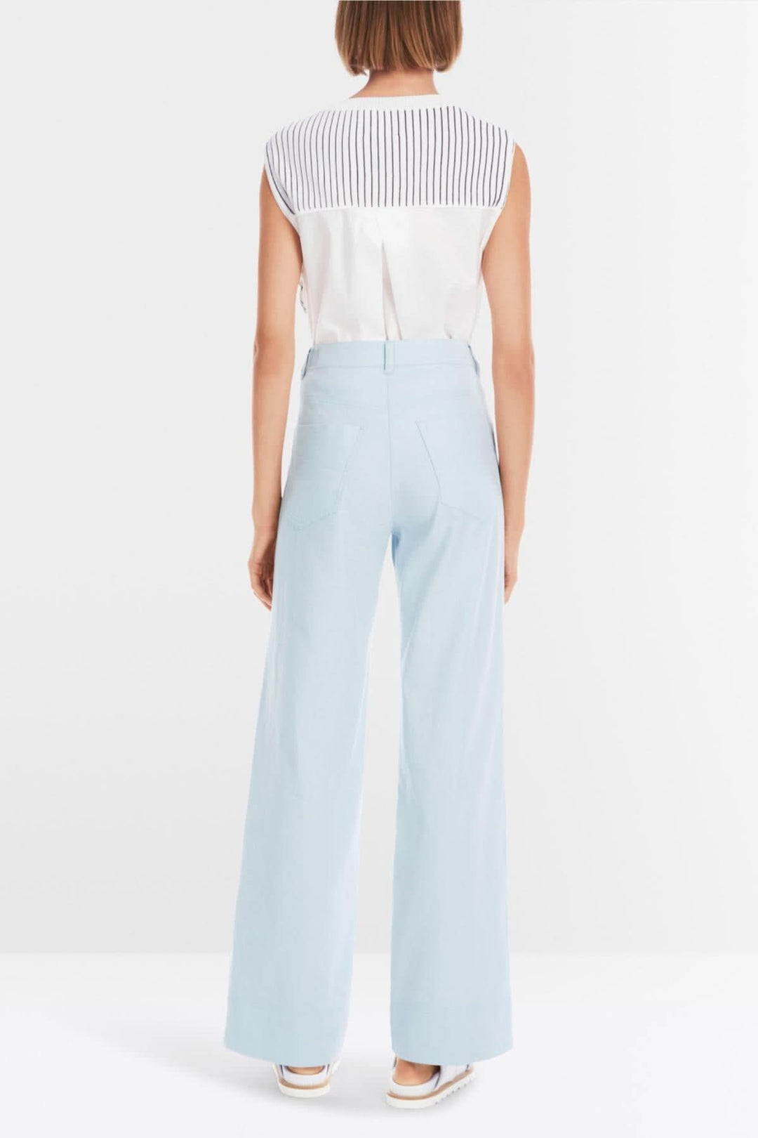Femme vue de dos portant le pantalon Faid bleu clair et un haut à rayures, style décontracté et estival.