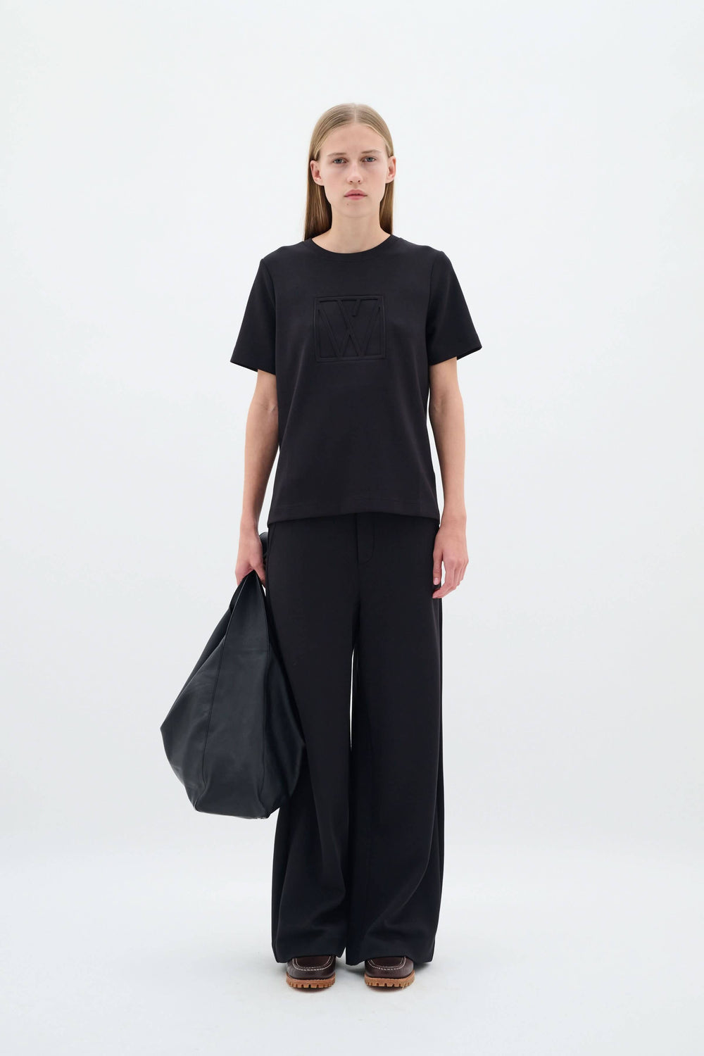 Femme portant un pantalon large et tee-shirt noir, avec un grand sac, dans un style élégant et décontracté.