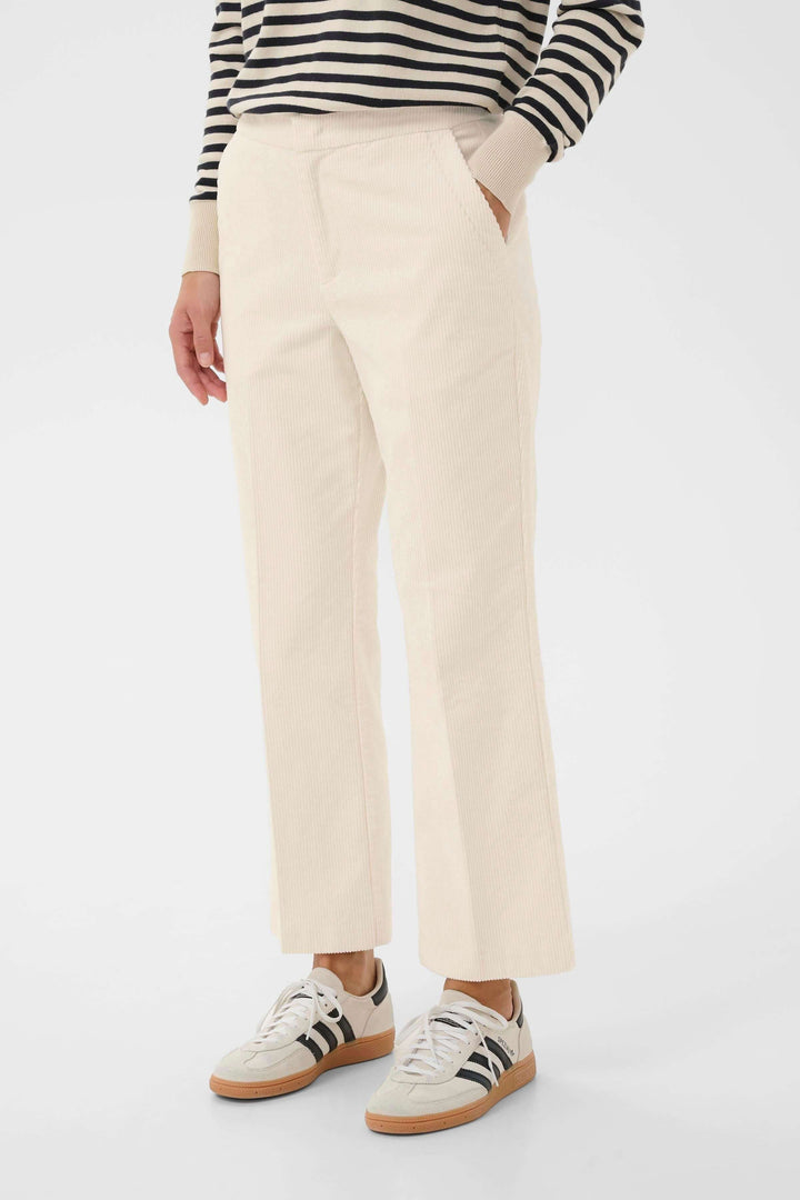 Pantalon en velours côtelé beige à coupe droite avec poches latérales, associé à un chandail rayé et des baskets.