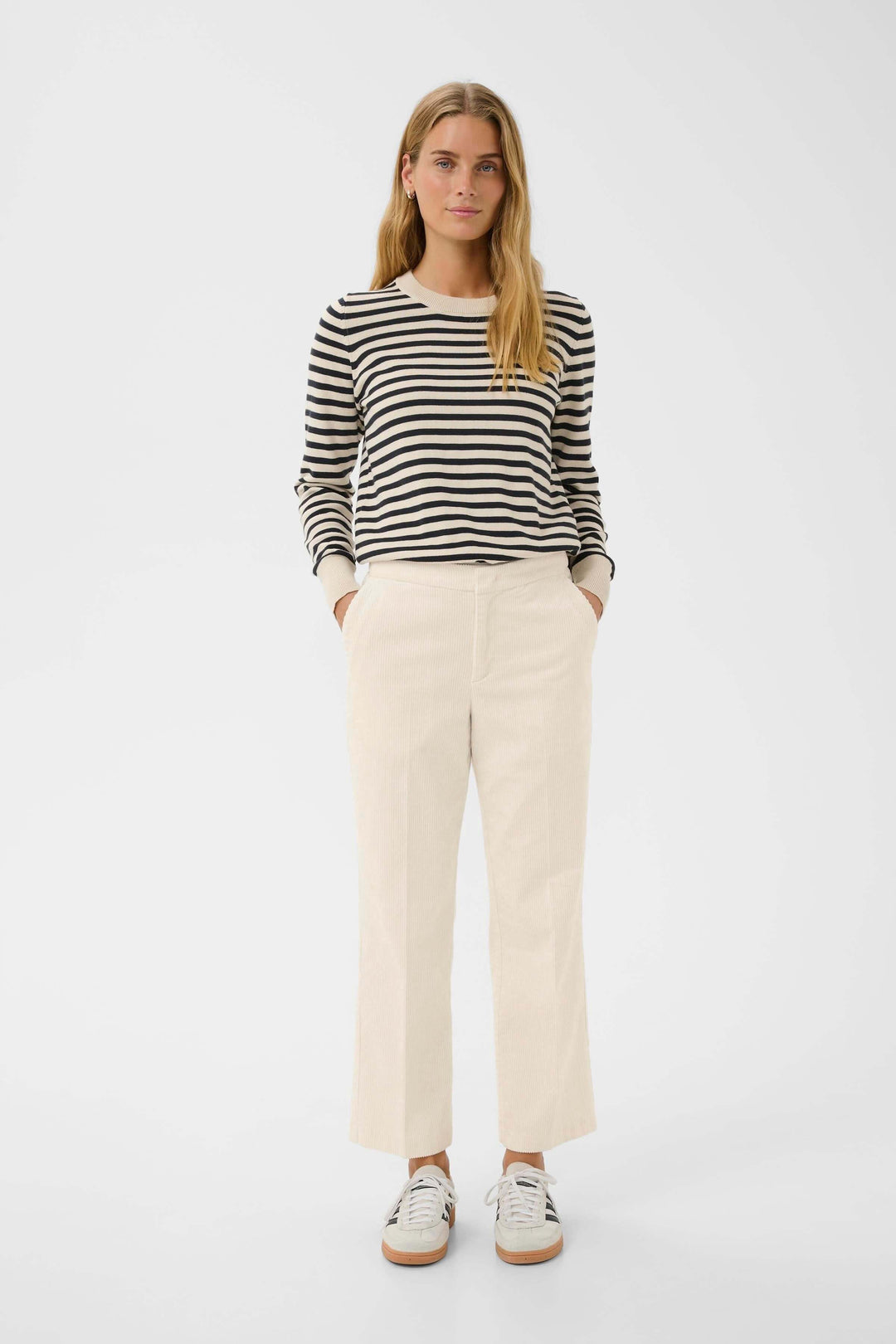Femme portant un pantalon en velours côtelé beige avec un chandail rayé noir et blanc, style décontracté chic.
