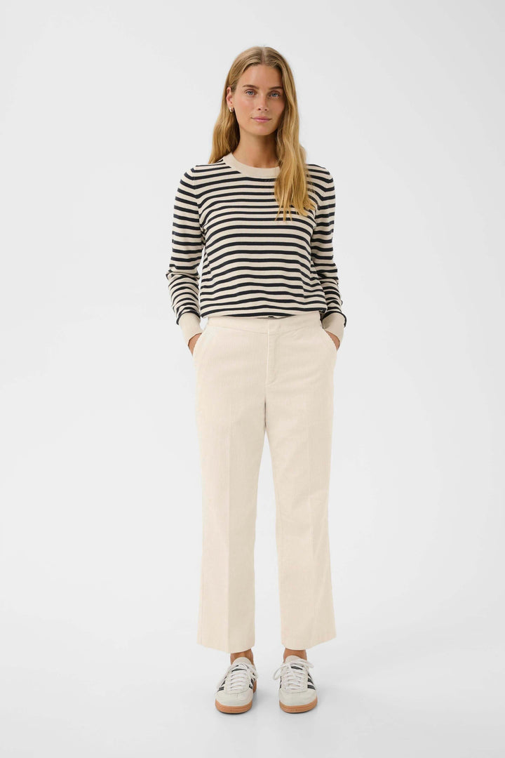 Femme portant un pantalon en velours côtelé beige avec un chandail rayé noir et blanc, style décontracté chic.