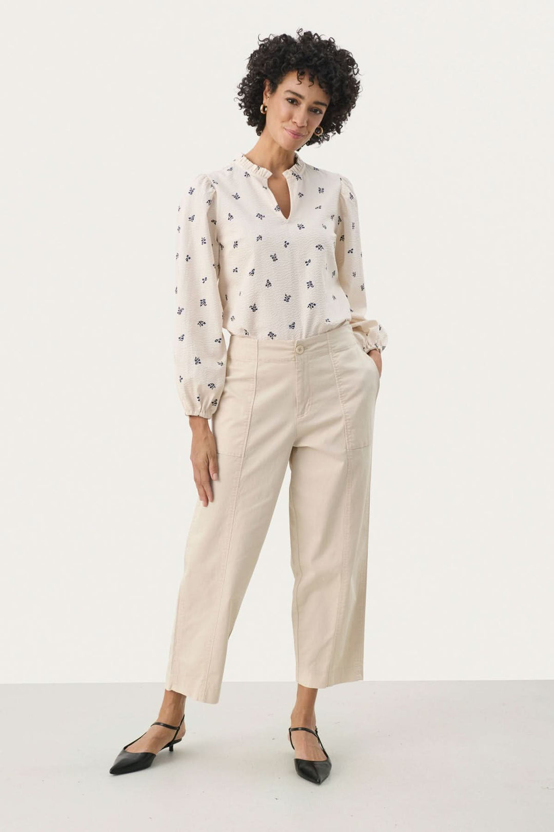Femme portant un pantalon Netta beige décontracté avec blouse imprimée et escarpins, style chic et moderne.