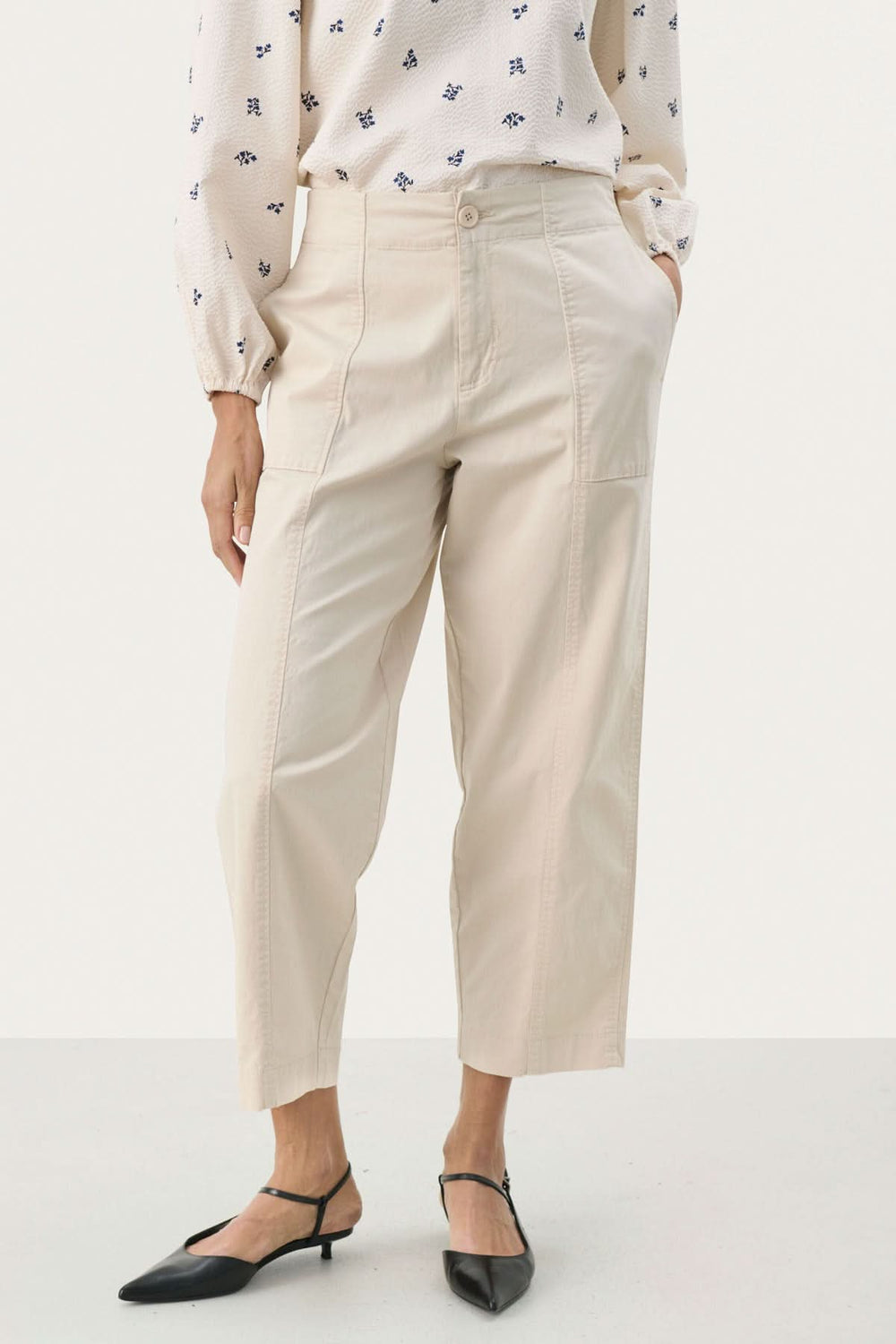 Pantalon Netta beige à coupe décontractée avec grandes poches et surpiqûres apparentes, porté avec une blouse fluide.