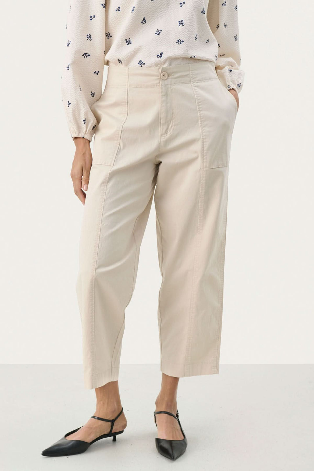 Pantalon Netta beige à coupe décontractée avec grandes poches et surpiqûres apparentes, porté avec une blouse fluide.